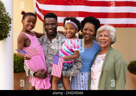 Portrait of smiling african american family with army father carrying daughters at entrance Stock Photo