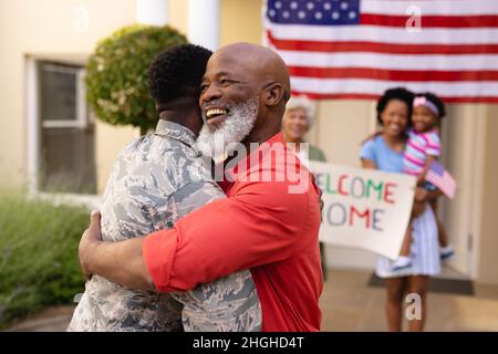 Happy african american senior bald man embracing army soldier against family Stock Photo