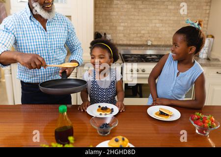 African american grandfather serving breakfast for his two granddaughters in kitchen at home Stock Photo