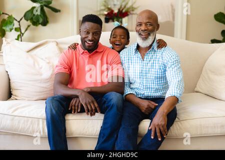 Portrait of african american grandfather, father and granddaughter smiling sitting on sofa at home Stock Photo