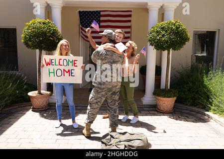 Caucasian boy hugging father in military uniform with family standing at entrance of house Stock Photo