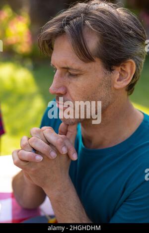 Close-up of caucasian man with eyes closed and hands clasped praying in garden Stock Photo