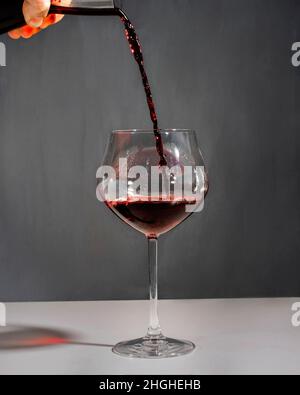 Red wine being poured from a decanter in a big glass with a neutral background. Stock Photo