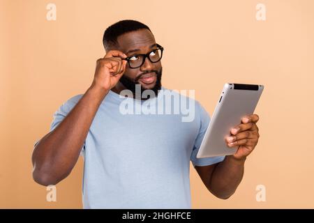 Portrait of attractive minded skilled guy using device gadget thinking reseach isolated over beige pastel color background Stock Photo