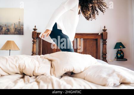 Unrecognizable young woman jumping on bed in bedroom Stock Photo