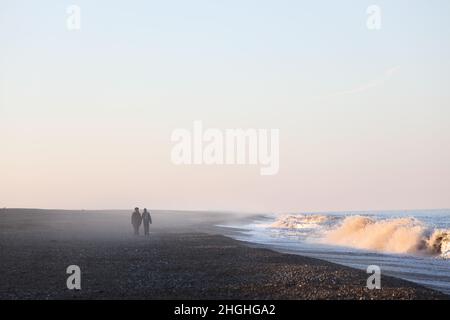 Two people walking hand in hand on a deserted beach surrounded by sea mist in Norfolk, England, UK Stock Photo