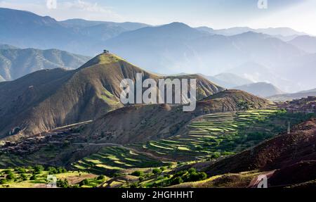 The Atlas Mountains in Morocco. Two solitary trees on top of a mountain overlook a village and terraced cultivated fields Stock Photo
