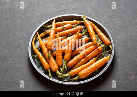 Roasted honey glazed carrots on plate over dark stone background. Close up view Stock Photo