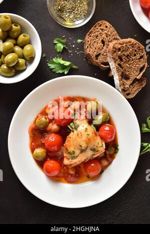 Cod stew with chickpeas, cherry tomatoes and olives on plate over dark stone background. Top view, flat lay Stock Photo