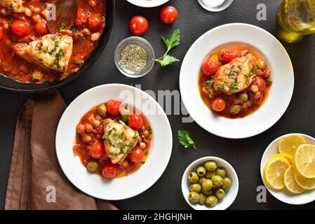 Cod stew with chickpeas, cherry tomatoes and olives over dark stone background. Top view, flat lay Stock Photo