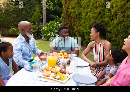 Happy african american family talking while sitting at dining table in backyard Stock Photo