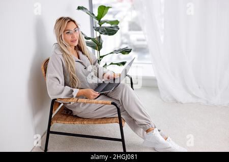 Adorable female freelancer in classic glasses searching information on social media websites for download files, happy blonde woman in spectacles usin Stock Photo