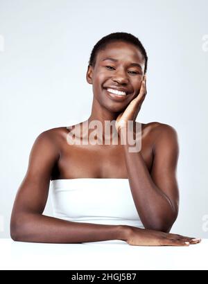 Her beauty radiates throughout. Studio portrait of a beautiful young woman feeling her skin against a grey background. Stock Photo