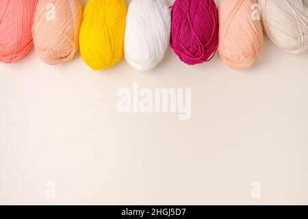 Colored balls of yarn is beige, burgundy, light pink, yellow  and white.  Skeins of yarn with empty space for your text or advertising on a beige back Stock Photo