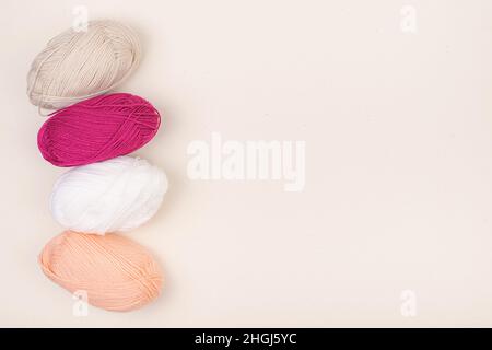 Colored balls of yarn is beige, light pink and white. Skeins of yarn with empty space for your text or advertising on a beige background. Stock Photo