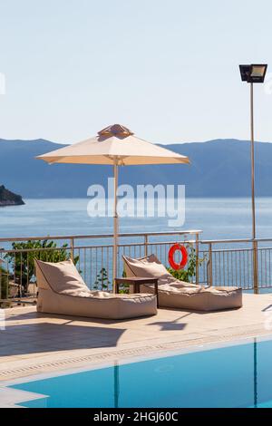 Luxury swimming pool with empty deck chairs or sunbeds and umbrella at resort with beautiful sea view Stock Photo