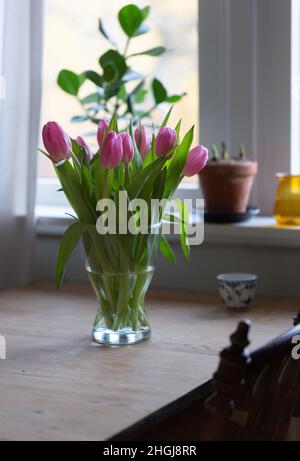 Tulips in a vase on a wooden table in front of window Stock Photo