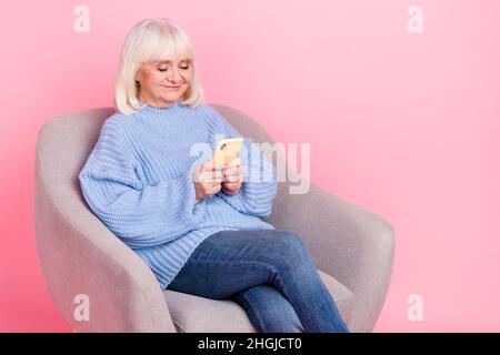 Portrait of attractive focused cheery grey-haired woman using gadget smm post app isolated over pink pastel color background Stock Photo