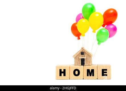 Word HOME made of wooden letter blocks and a miniature house model with toy balloons isolated on white background. Post-moving housewarming party conc Stock Photo