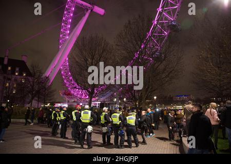 Police officers watch participants gathering for a freedom rally against Covid-related measures such as vaccine passports near London Eye on Southbank Stock Photo