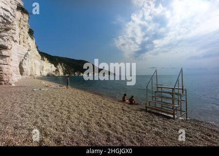 Vignanotica beach, Gargano, Puglia, Italy: two women and a man stand on the deserted beach chatting close the high white cliff of Vignanotica Stock Photo