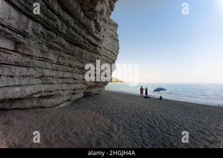 Vignanotica beach, Gargano, Puglia, Italy: a woman is photographing a man near an umbrella on the deserted beach close the high cliff of Vignanotica Stock Photo