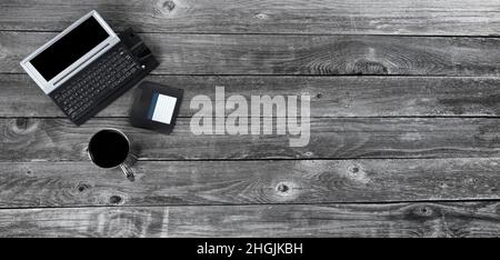Aged wood office desk table with retro technology of a portable computer, data disk and coffee in steel mug. Top view with plenty of copy space in fla Stock Photo