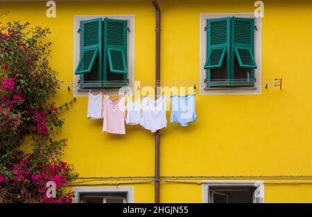 Colorful laundry hangs to dry against an ancient, colorful, yellow wall of a home with beautiful bougainvilleas in Riomaggiore, one of five ancient, p Stock Photo