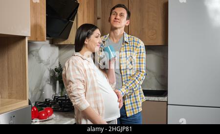 Pregnant woman drinks tea and husband strokes belly softly Stock Photo