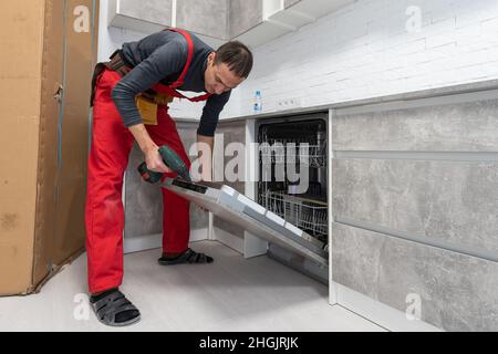 Young Repairman Service Worker Repairing Dishwasher Appliance In Kitchen. Stock Photo