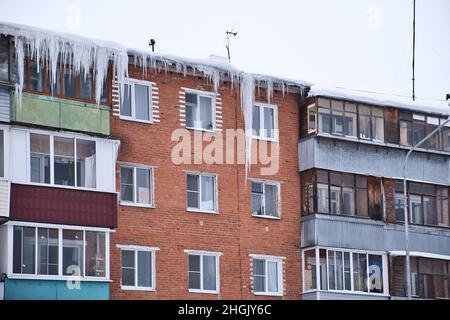 Giant icicles hanging down from the roof of an old residential brick house. Dangerous icicles hangs from the roof. Harsh nord winter. Stock Photo