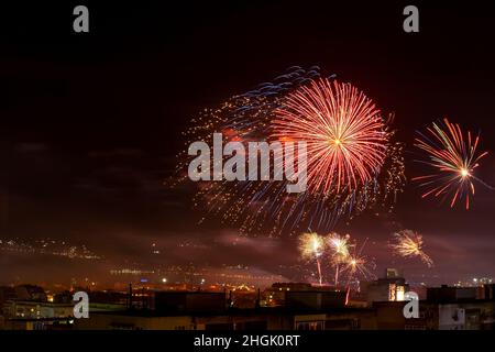 Red blue bright fireworks in the night sky over a city. Townspeople celebrating the New Year and launching fireworks at midnight. Outdoor night scene. Stock Photo