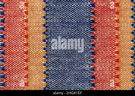 Macro texture of plain weave fabric. Striped cloth background of red, blue, orange and white colors. Textile canvas surface close-up. Design element. Stock Photo