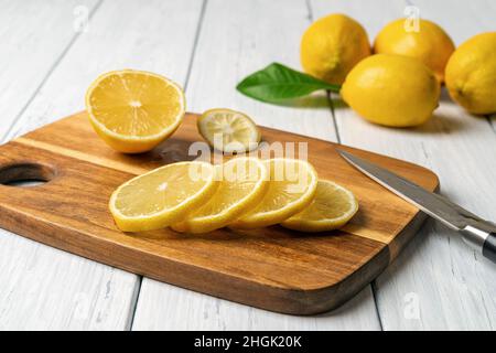 Fresh juicy lemon slices on a cutting board over white wooden table. Cutting citruces with a knife. Raw lemons for superfood and antioxidant concepts. Stock Photo