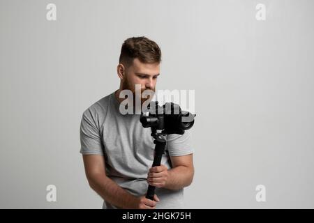 Professional bearded videographer holding camera which set on 3-axis gimbal. Videographer using steadicam. Pro equipment helps to make high quality Stock Photo