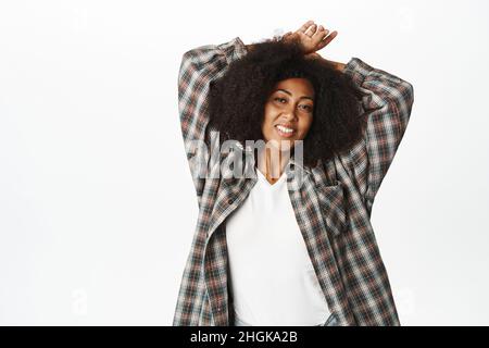 Carefree young african woman, feeling free and healthy, smiling happy, stretching arms up, posing against white background Stock Photo