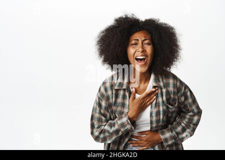 Portrait of beautiful carefree african woman, laughing and smiling joyful, watching smth funny, standing over white background Stock Photo