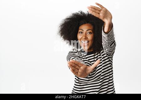 Beautiful and happy Black woman looking through hand frames and smiling, imaging smth, making photo, shooting smth, searching inspiration, standing Stock Photo