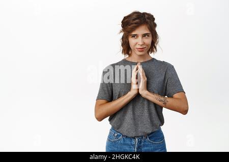Sneaky young woman planning, scheming something devious, steeple fingers and smirking pleased, has an idea, plan, standing over white background with Stock Photo