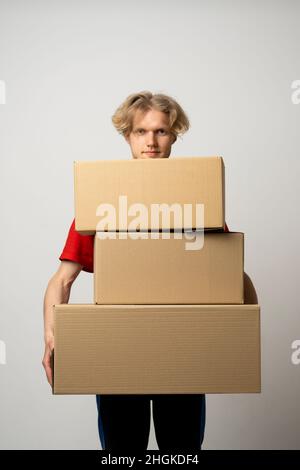 Cheerful delivery man. Happy young courier holding a cardboard boxes and smiling while standing against white background. Delivery man holding pile of Stock Photo