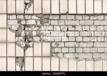 Destruction of the wall facade with falling off lined rectangular facade tiles and exposed fragments of silicate brick. Copy space. Stock Photo