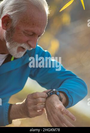 Portrait of a senior man using smart watch while exercise in tracksuit Stock Photo