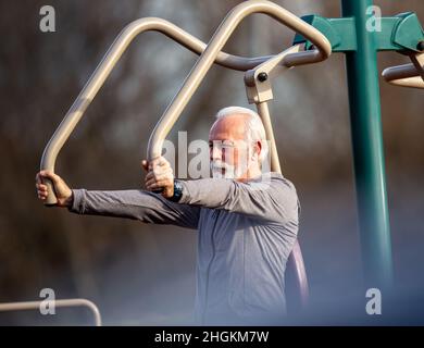 Senior man in tracksuit exercising at public gym outdoor in spring time Stock Photo