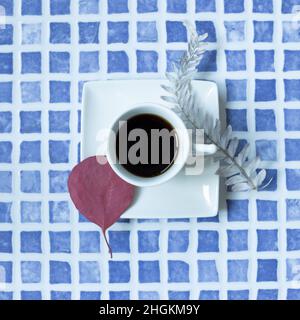 Cup of coffee with dry plant decor on blue ceramic mosaic table. top view Stock Photo