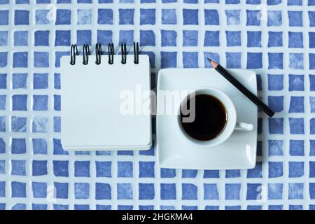 Blank white notepad and cup of coffee on blue ceramic mosaic table. top view, copy space Stock Photo