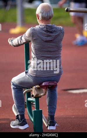 Back view of a senior man in tracksuit working out in public gym Stock Photo