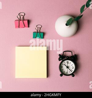 Memo pad, clip, clock, vase of green leaf on pink background. workspace. flat lay, top view, copy space Stock Photo