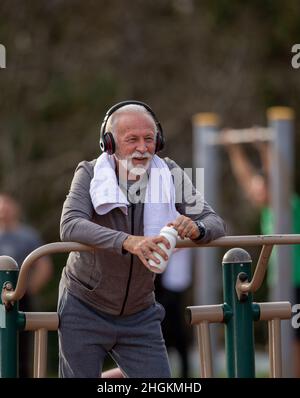 Senior man with headphones holding a bottle of water in his hand while making a break from exercise at outdoor gym Stock Photo