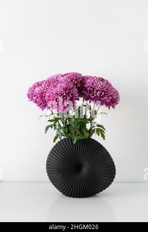 Stylish composition of the beautiful pink chrysanthemum flowers standing in black modern vase at the table. Lagom Swedish Culture concept Stock Photo