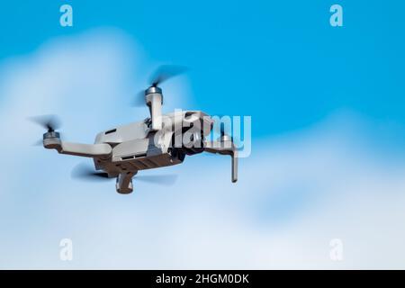 Kharkiv, Ukraine - March 6, 2021: Dji Mavic Mini 2 drone, flying in sunny blue daylight. New quadcopter device hovering on blurry white clouds sky bac Stock Photo